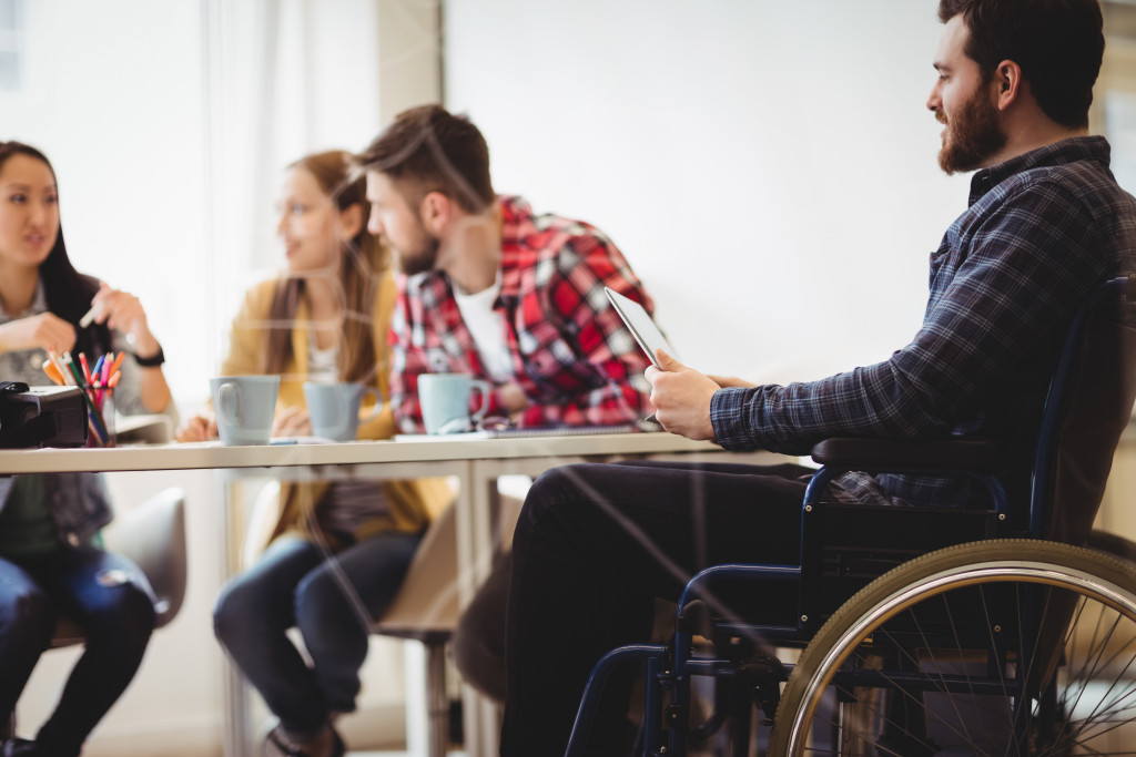 A worker sitting on a wheelchair in a conference room with other co-workers